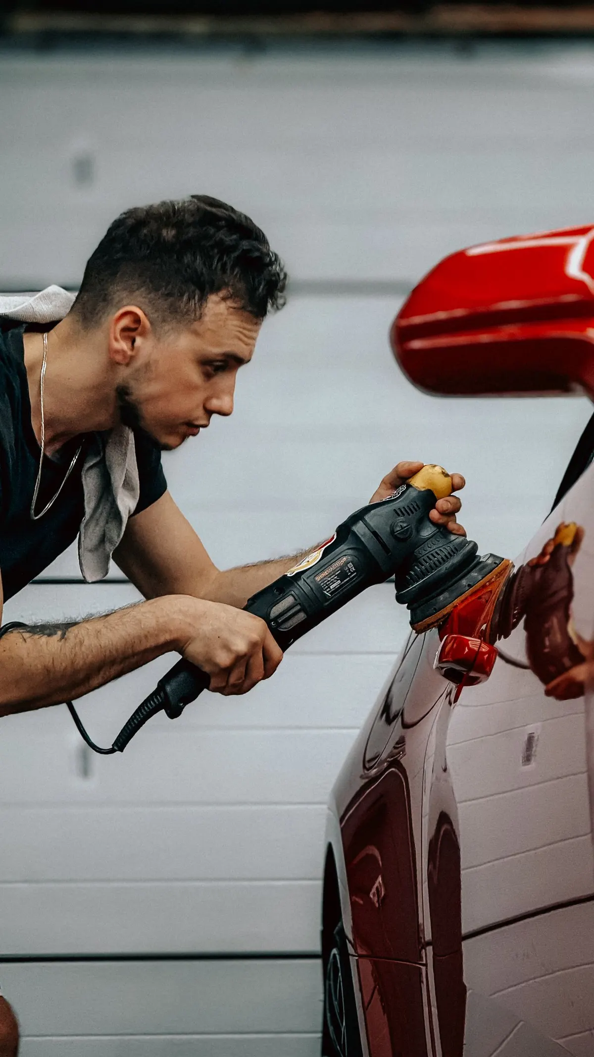 Car detailer polishing a red car in a garage